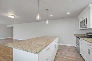 Kitchen featuring light stone countertops, appliances with stainless steel finishes, decorative light fixtures, white cabinets, and a center island