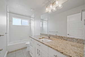 Full bathroom with tile patterned floors, a textured ceiling, toilet, vanity, and tiled shower / bath