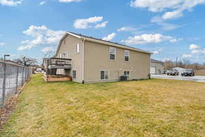 Back of house with a lawn, a wooden deck, cooling unit, and a garage