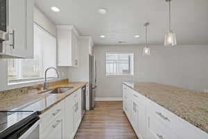 Kitchen with white cabinetry, light stone countertops, sink, pendant lighting, and appliances with stainless steel finishes