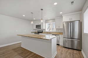 Kitchen with white cabinets, a center island, light stone counters, and stainless steel appliances