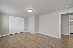 Unfurnished bedroom featuring a textured ceiling, light wood-type flooring, and a closet