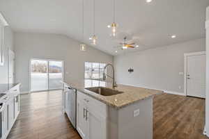 Kitchen with light stone counters, stainless steel dishwasher, sink, white cabinetry, and an island with sink