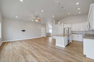 Kitchen featuring stainless steel appliances, ceiling fan, decorative light fixtures, white cabinets, and an island with sink