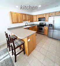 Kitchen featuring a kitchen breakfast bar, sink, a textured ceiling, kitchen peninsula, and stainless steel appliances