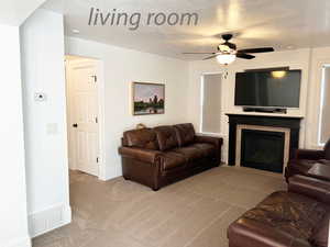 Living room with a tile fireplace, light carpet, ceiling fan, and a textured ceiling