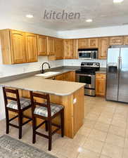 Kitchen with sink, appliances with stainless steel finishes, light tile patterned flooring, a kitchen bar, and kitchen peninsula