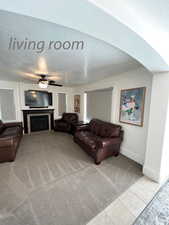 Living room with a tile fireplace, light carpet, a textured ceiling, and ceiling fan