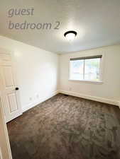 Empty room with dark colored carpet and a textured ceiling