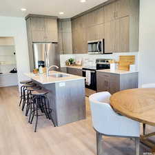 Kitchen featuring sink, stainless steel appliances, light hardwood / wood-style floors, a breakfast bar area, and a center island with sink