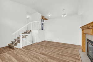 Unfurnished living room with vaulted ceiling, wood-type flooring, a tile fireplace, and an inviting chandelier