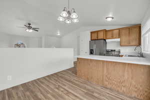 Kitchen with pendant lighting, ceiling fan with notable chandelier, sink, light hardwood / wood-style flooring, and stainless steel appliances