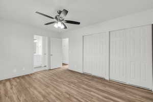 Unfurnished bedroom with ensuite bath, ceiling fan, multiple closets, and light wood-type flooring