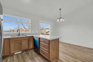 Kitchen featuring dishwasher, sink, an inviting chandelier, kitchen peninsula, and pendant lighting