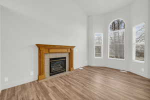 Unfurnished living room with a tiled fireplace, a healthy amount of sunlight, lofted ceiling, and light hardwood / wood-style floors