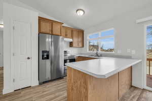 Kitchen featuring kitchen peninsula, appliances with stainless steel finishes, light wood-type flooring, vaulted ceiling, and sink