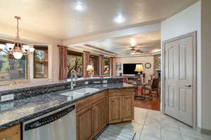 Kitchen with sink, hanging light fixtures, a raised ceiling, stainless steel dishwasher, and dark stone countertops