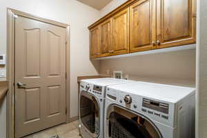 Washroom with cabinets, light tile patterned floors, and washing machine and dryer