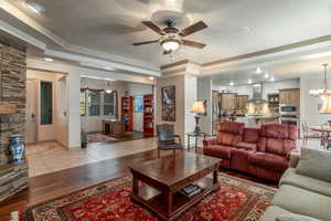 Living room with ceiling fan with notable chandelier, a tray ceiling, and light hardwood / wood-style flooring