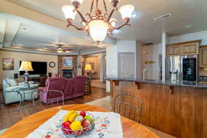 Dining room featuring sink, light hardwood / wood-style flooring, a tray ceiling, a fireplace, and ceiling fan with notable chandelier