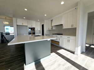 Kitchen with built in microwave, sink, premium range hood, an island with sink, and white cabinets