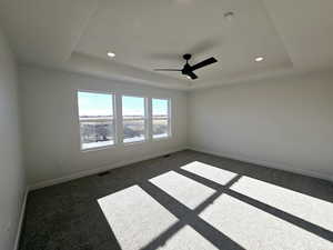 Unfurnished room with dark colored carpet, ceiling fan, and a tray ceiling