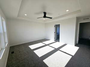 Unfurnished room with dark colored carpet, a tray ceiling, and ceiling fan