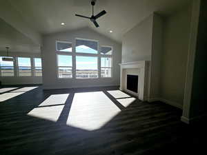 Unfurnished living room featuring ceiling fan, dark hardwood / wood-style flooring, vaulted ceiling, and a brick fireplace