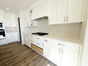 Kitchen with white cabinetry, stainless steel gas cooktop, backsplash, oven, and custom range hood