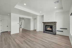 Unfurnished living room with a stone fireplace, a tray ceiling, and light hardwood / wood-style flooring