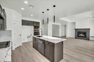 Kitchen with a kitchen island with sink, hanging light fixtures, a fireplace, light stone counters, and stainless steel appliances