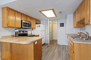 Kitchen with sink, light hardwood / wood-style flooring, a textured ceiling, appliances with stainless steel finishes, and kitchen peninsula