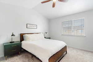 Carpeted bedroom featuring vaulted ceiling and ceiling fan