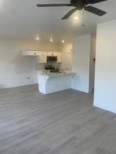 Kitchen featuring a kitchen breakfast bar, light wood-type flooring, white cabinetry, kitchen peninsula, and stainless steel appliances