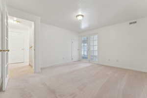 Unfurnished room with a textured ceiling, light carpet, and french doors