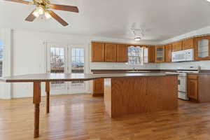 Kitchen with ceiling fan, a center island, white appliances, and light hardwood / wood-style flooring