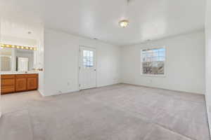 Unfurnished bedroom with connected bathroom, sink, light colored carpet, and multiple windows