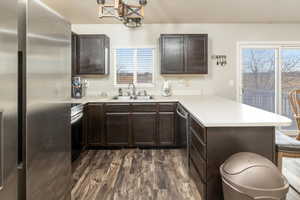 Kitchen featuring kitchen peninsula, appliances with stainless steel finishes, dark brown cabinetry, dark wood-type flooring, and sink