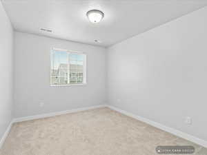 Empty room featuring a textured ceiling and light colored carpet