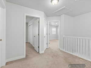 Hall featuring a textured ceiling and light colored carpet