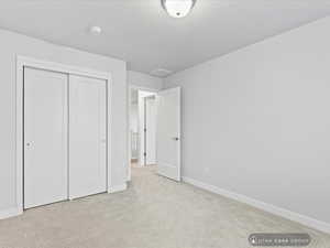 Unfurnished bedroom featuring light colored carpet, a textured ceiling, and a closet