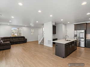 Kitchen with sink, light hardwood / wood-style flooring, stainless steel fridge, a kitchen island with sink, and dark brown cabinets