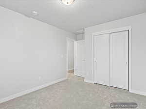 Unfurnished bedroom featuring light carpet, a closet, and a textured ceiling