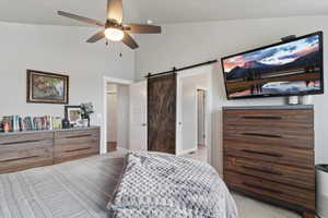 Carpeted bedroom with a barn door, ceiling fan, and vaulted ceiling