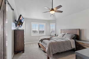 Bedroom featuring a barn door, ceiling fan, light carpet, and a textured ceiling