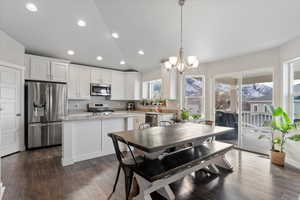 Kitchen featuring appliances with stainless steel finishes, dark hardwood / wood-style flooring, pendant lighting, white cabinets, and a center island