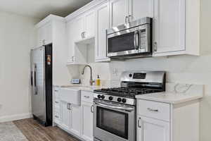 Kitchen featuring light stone counters, sink, white cabinets, and stainless steel appliances