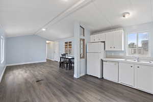 Kitchen featuring white appliances, sink, vaulted ceiling, dark hardwood / wood-style flooring, and white cabinetry