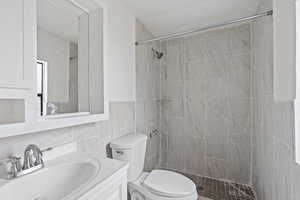 Bathroom with tasteful backsplash, vanity, tiled shower, tile walls, and toilet