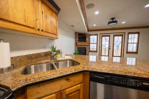 Kitchen featuring stainless steel dishwasher, a stone fireplace, sink, and crown molding